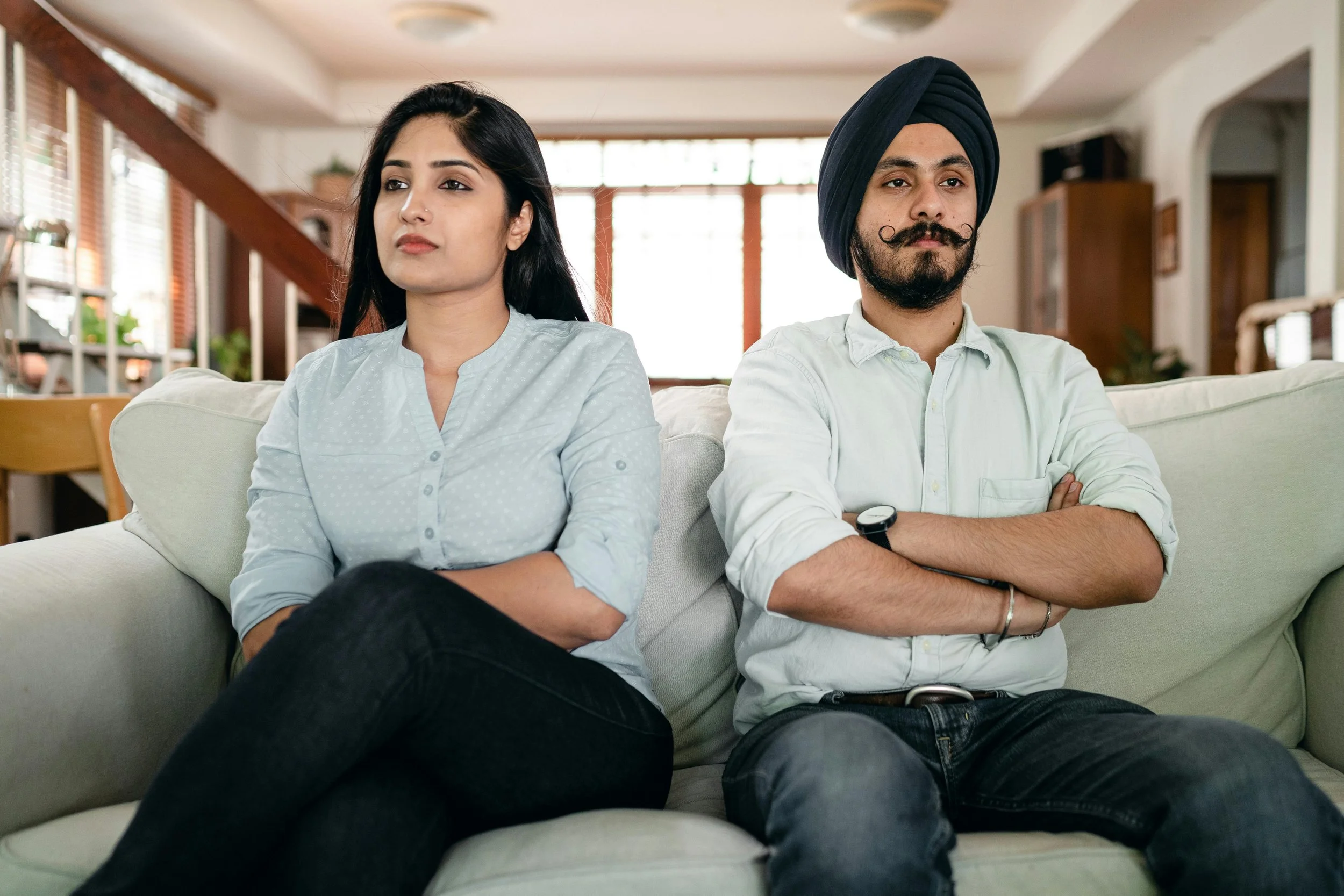 A couple sitting apart with closed body language, symbolizing the tension and disconnect created by silent treatment and other unhealthy communication patterns.