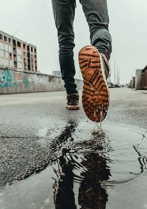 A close-up shot of a person walking through a puddle on an urban street, symbolizing the journey, challenges, and forward movement associated with stepping into adulthood and personal growth.