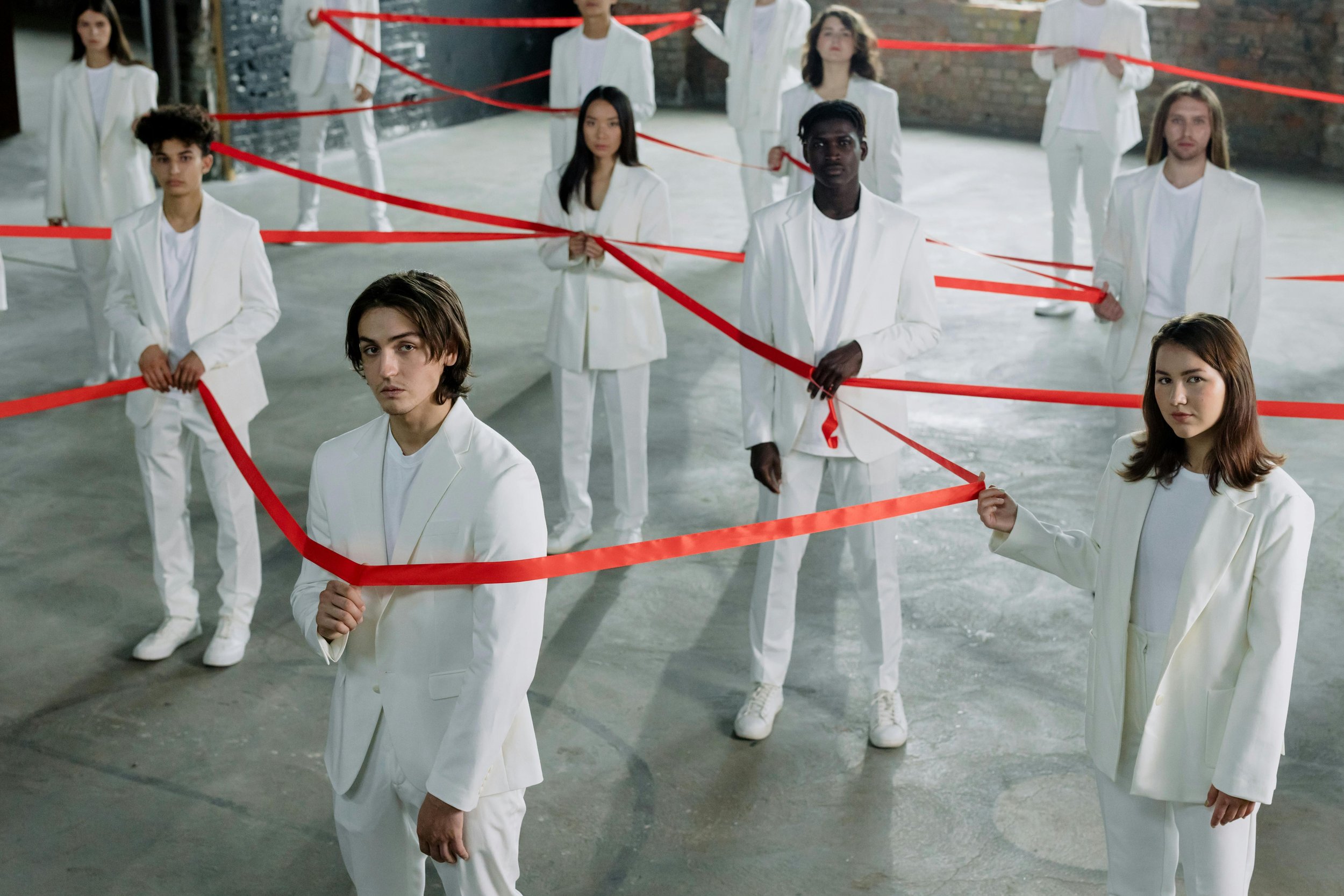 People standing connected by red ribbons, symbolizing the intersecting identities and layered experiences explored in psychodynamic therapy for LGBTQ individuals.