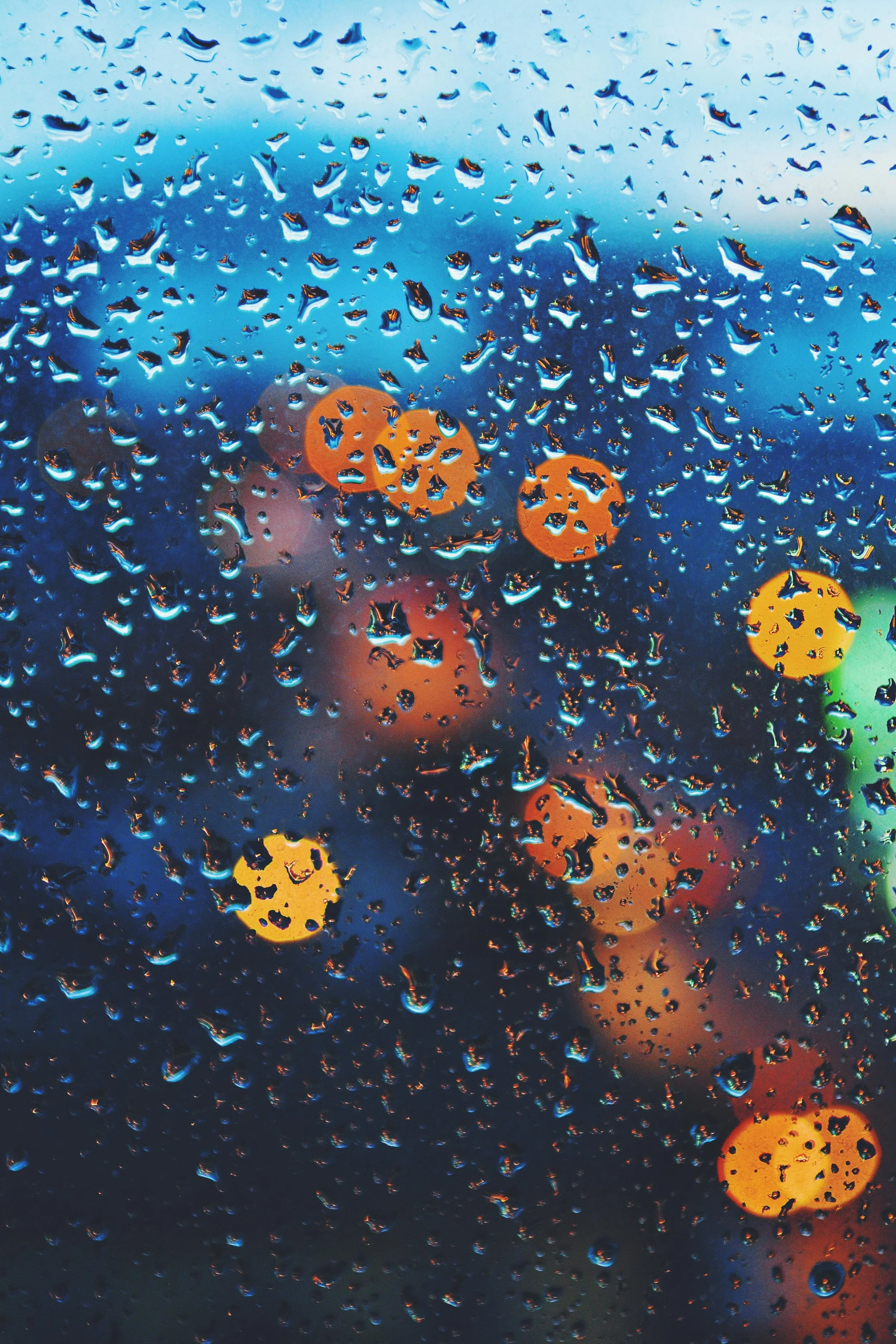 Raindrops on a window with blurred city lights behind it, symbolizing the emotional heaviness and quiet reflection that can follow coming out.