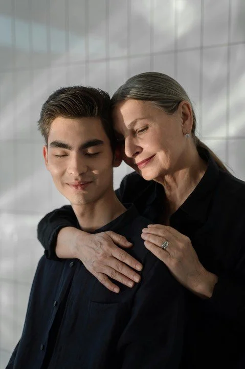 Adult son with eyes closed while older mother embraces him from behind, representing complex parent-child dynamics, emotional closeness, and boundary challenges addressed in therapy for men in San Francisco.