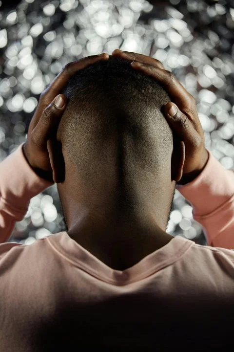 Man holding his head with both hands against a blurred background, symbolizing emotional overwhelm, self-sabotage, internal conflict, and self-defeating patterns explored in therapy for men in San Francisco