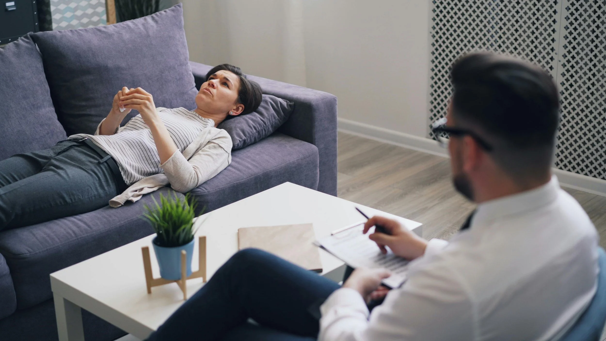 A person lying on a therapy couch while a therapist takes notes, symbolizing the exploration of transference and relational patterns in psychodynamic treatment.