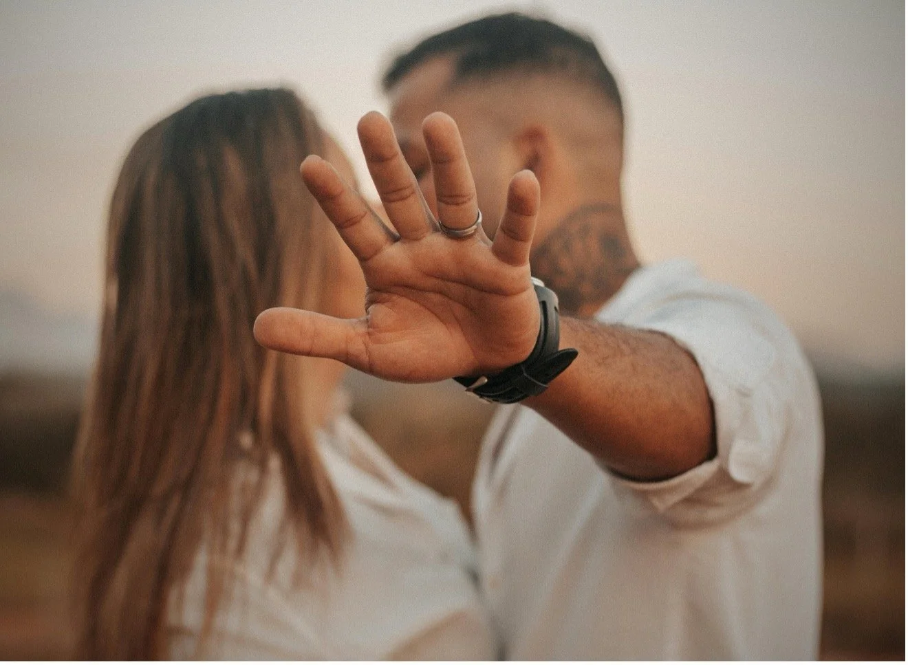 A couple standing close together while one person raises their hand toward the camera in a blocking gesture, symbolizing emotional distance, conflict, or the need for boundaries in relationships.