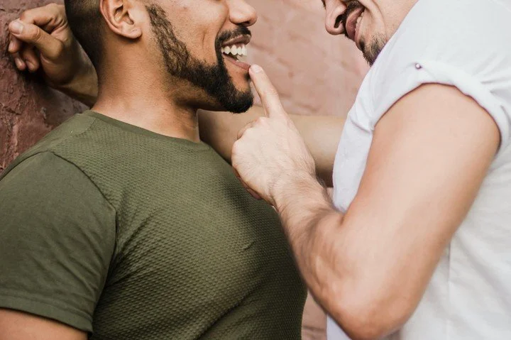 Two men sharing a close and intimate moment, smiling and touching, representing emotional and physical connection in relationships explored in therapy for gay men in San Francisco.