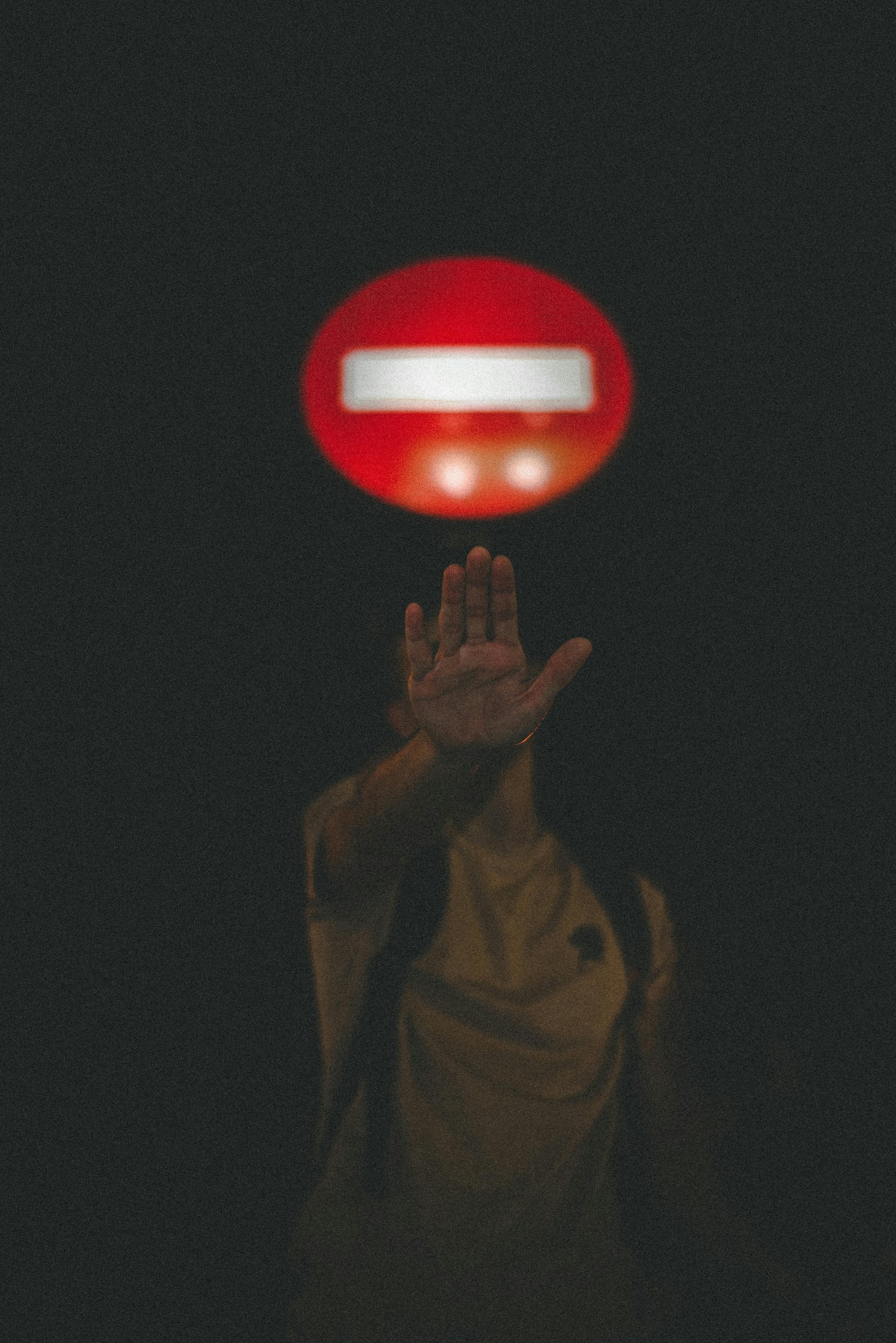 A person holding up a hand in a stopping gesture beneath a glowing red sign, symbolizing the act of setting boundaries and ending people-pleasing behaviors.