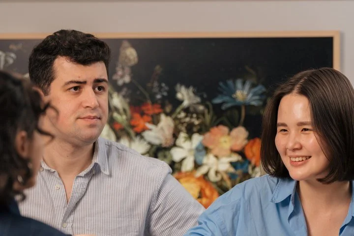 Three adults sharing a meal and interacting at a dinner table, illustrating social connection and the experience of adapting oneself to others