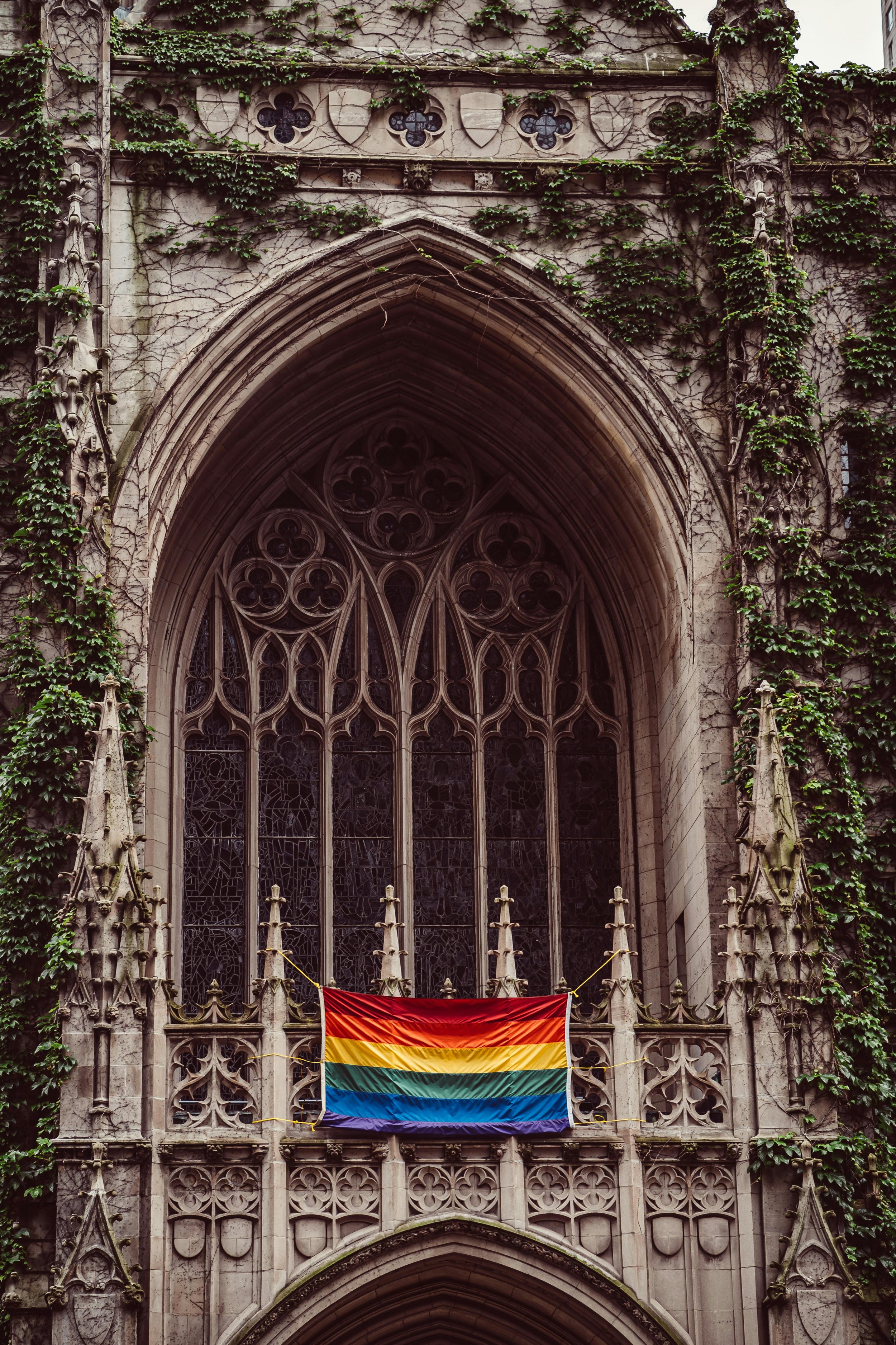 A rainbow flag displayed on a gothic church façade, symbolizing the intersection of LGBTQ identity, religion, and the journey of healing from spiritual trauma.