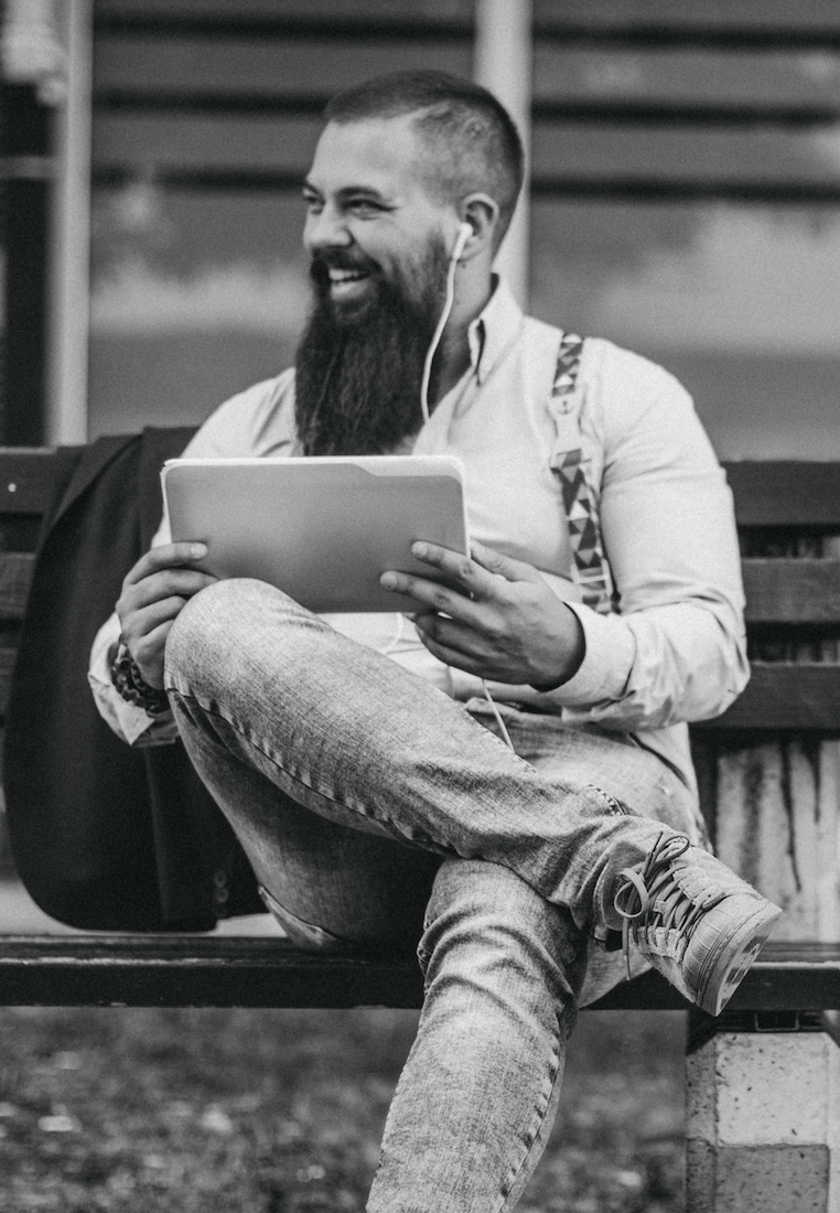A man sitting on a bench smiling while using a tablet, symbolizing the reflection and renewed perspective therapy can bring during midlife transitions.
