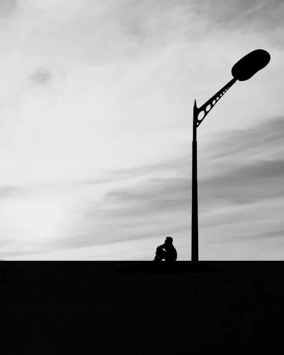 Silhouette of a solitary person sitting beneath a streetlight against a vast sky, symbolizing loneliness, emotional connection, intimacy, self-worth, and the difference between being desired and being truly known.