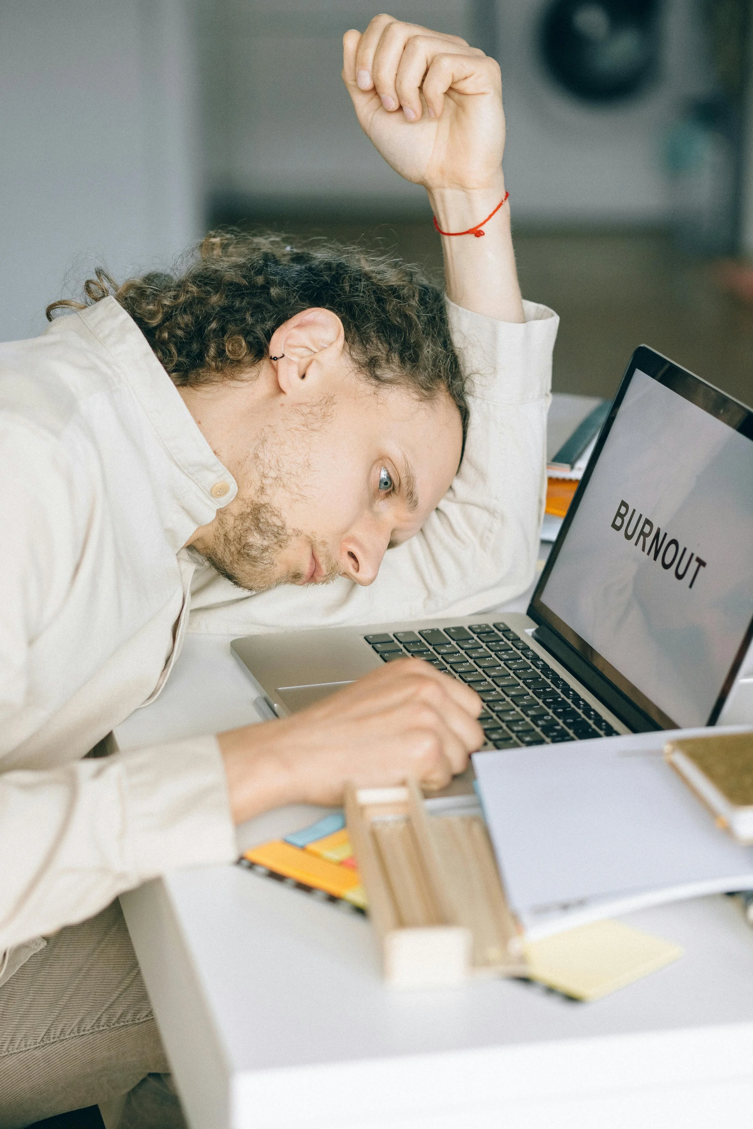 A man lying exhausted over his laptop with the word “BURNOUT” on the screen, symbolizing the overwhelming impact of career pressure and work stress on men’s mental health.