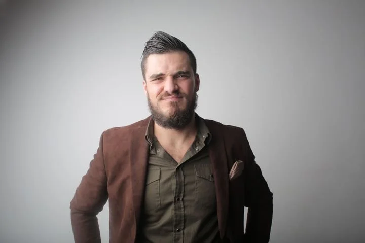 Man with a skeptical expression reacting to praise, representing self-doubt, difficulty accepting compliments, low self-worth, and men's mental health concerns addressed in therapy in San Francisco.