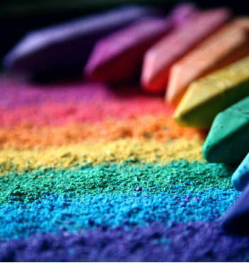 Rainbow-colored chalk on a textured surface, symbolizing the diversity and complexity involved in coming out across different family cultures and generations.