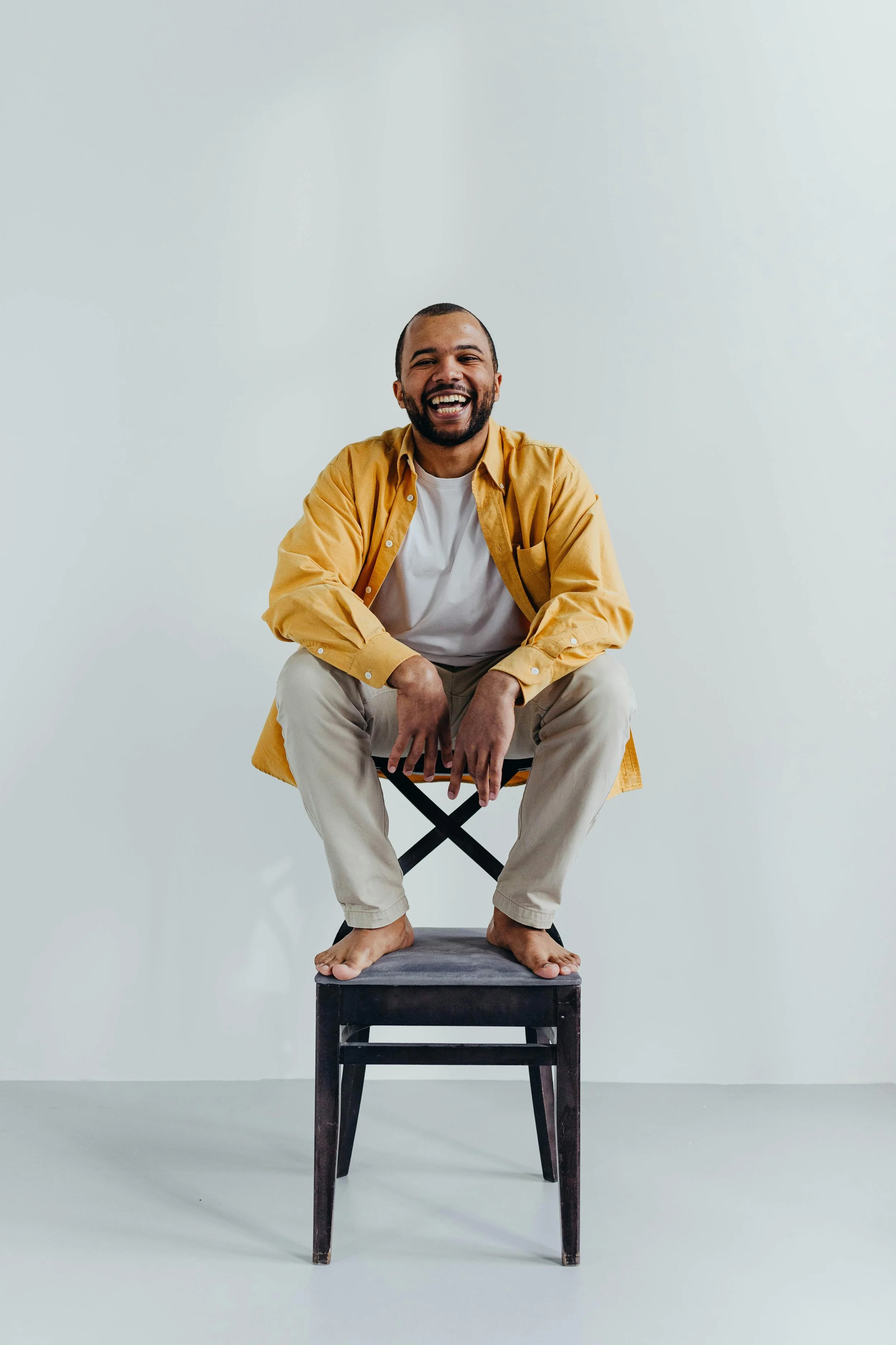 A young adult sitting barefoot and smiling confidently on a stool, symbolizing openness, readiness, and curiosity when considering starting therapy.