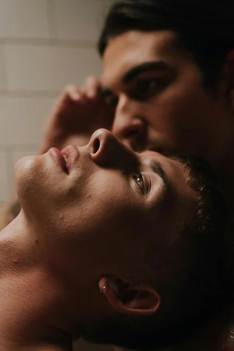 Two men lying closely together, one appearing deep in thought while the other gently leans in, symbolizing reflection, emotional intimacy, and learning from past relationship patterns.