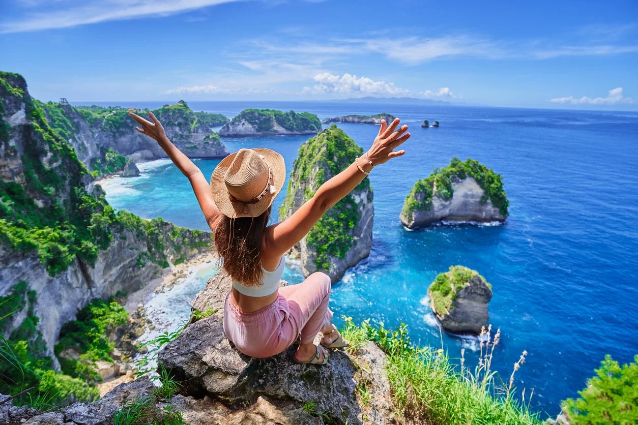 woman in hat looking out over beautiful view of blue ocean with rock pillars