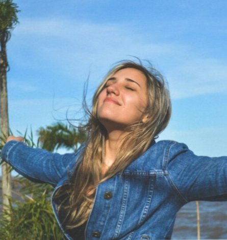 Woman with arms outstretched, smiling against a blue sky and water backdrop.