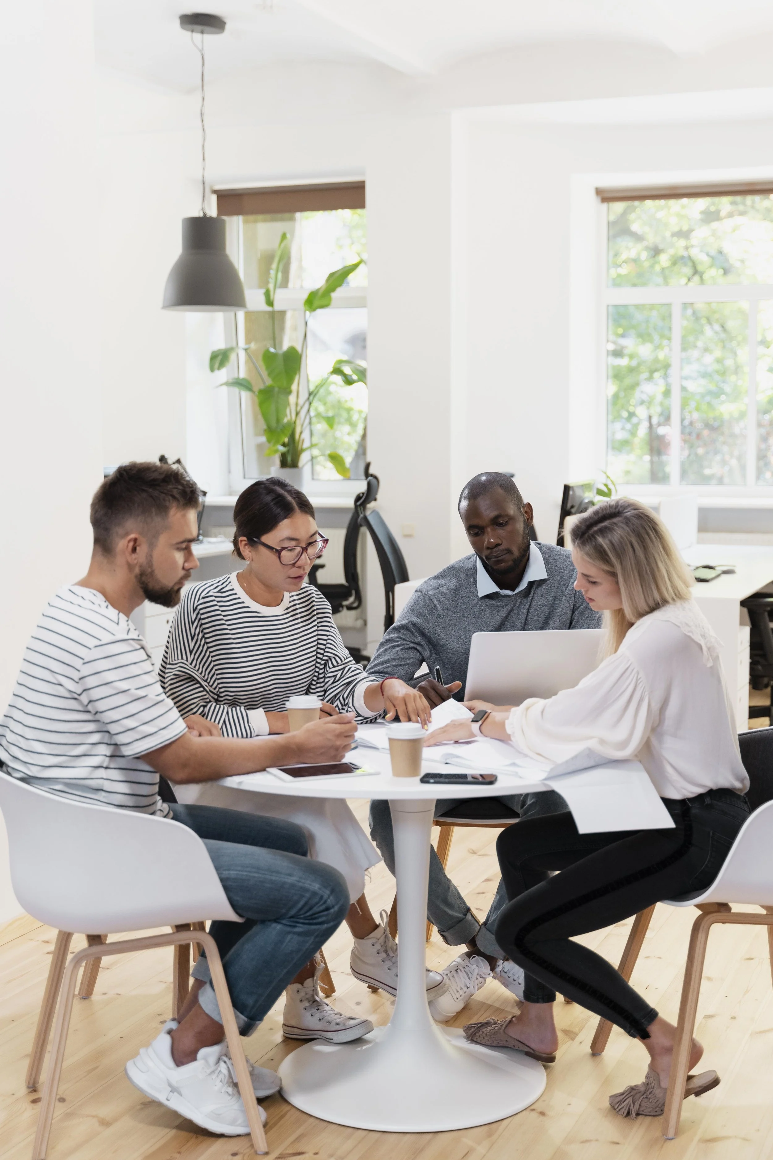 Four people sitting around a white table engaged in a discussion, with coffee cups and papers.