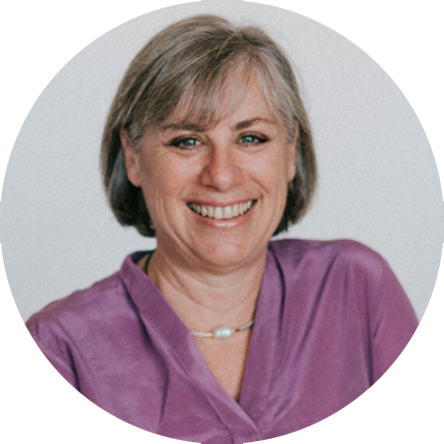 Smiling woman with short gray hair wearing a purple top against a light background.