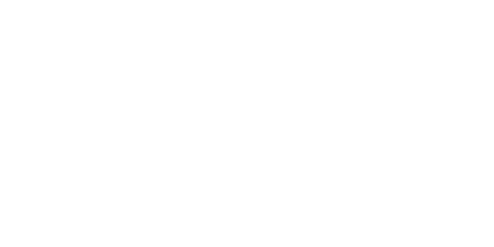 A person taking a photo of a sunset over the ocean from a rocky shoreline.