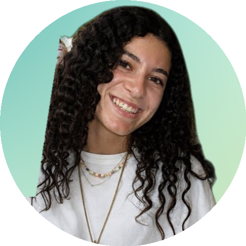 Young woman with dark brown hair smiling, wearing a white shirt and two necklaces, against a light green background.