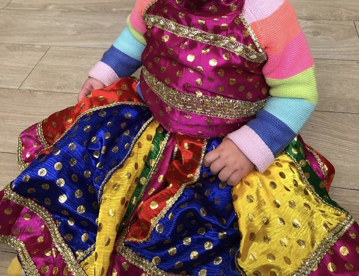Child wearing colorful, traditional dress with gold polka dots and trim, sitting on a wooden floor for a Bollywood Dance Incursion.