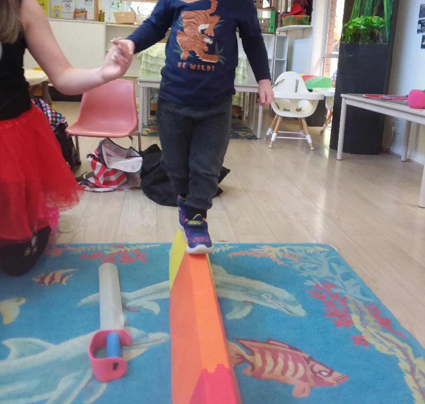 Child balancing on a foam beam, indoors, with guidance from an educator