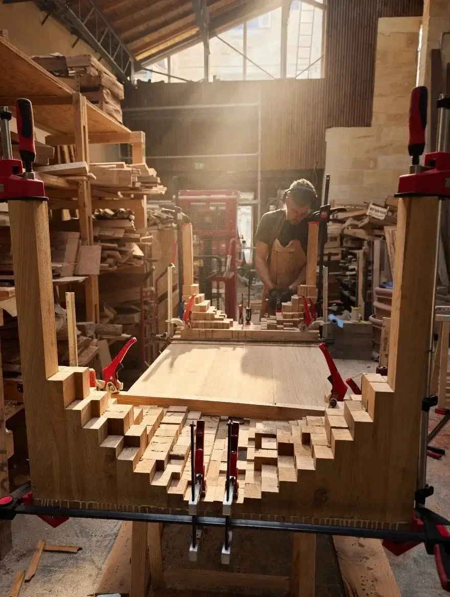 Les coulisses de la fabrication artisanale de la table en bois massif Bamba. La table est à l'envers, l'ébéniste façonne la table à la main