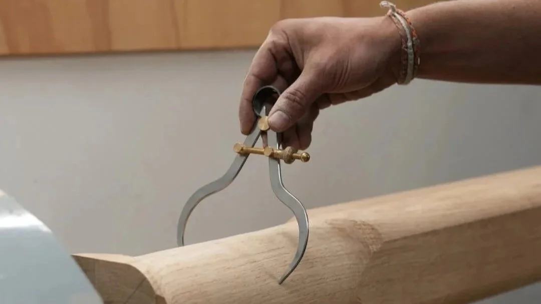La main d'un ébéniste qui tient un outil de mesure pour prendre les dimensions d'un morceau de bois installé sur un tour à bois