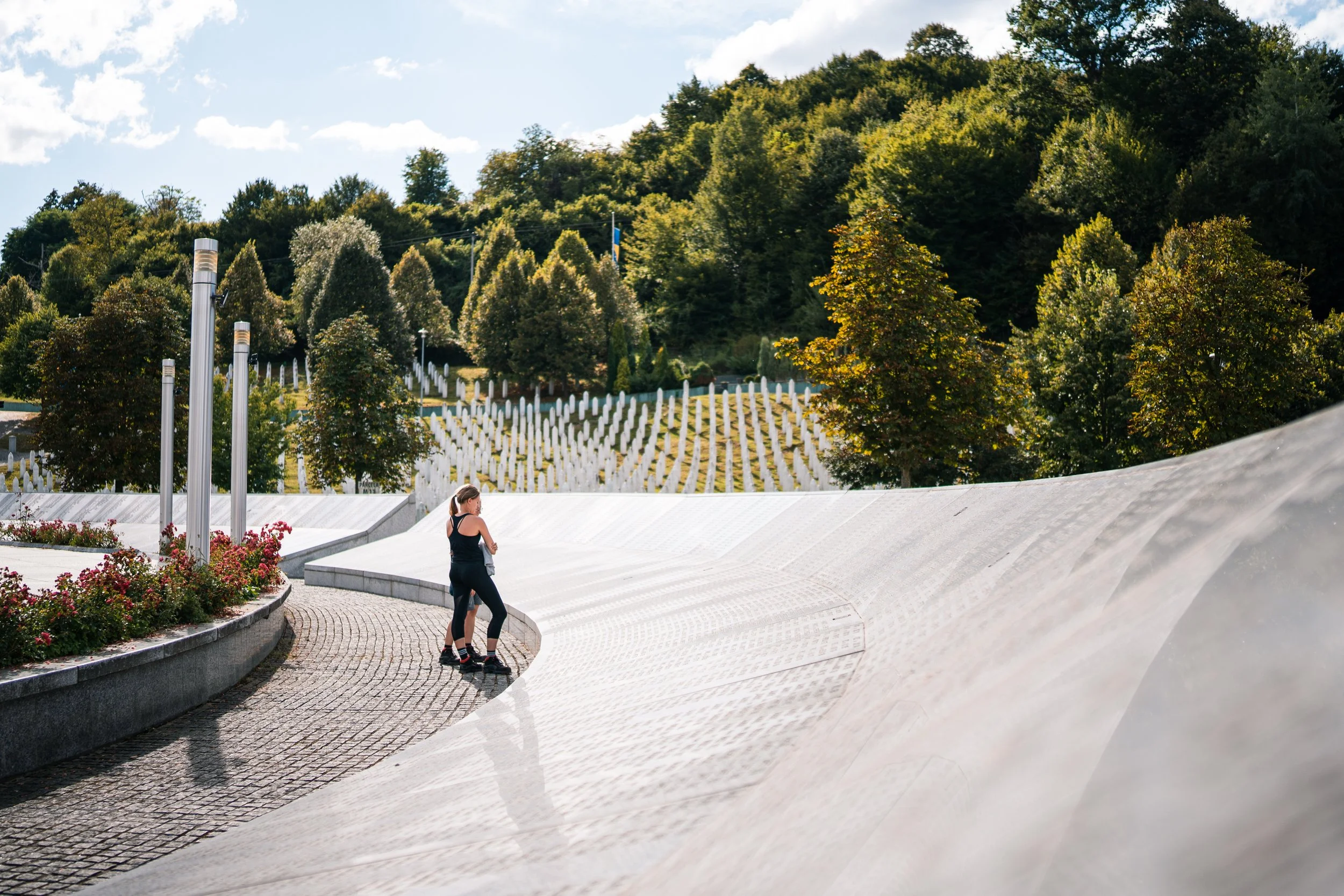 Woman walking at the Srebrenica Memorial in Bosnia and Herzegovina, with rows of white grave markers in the background.