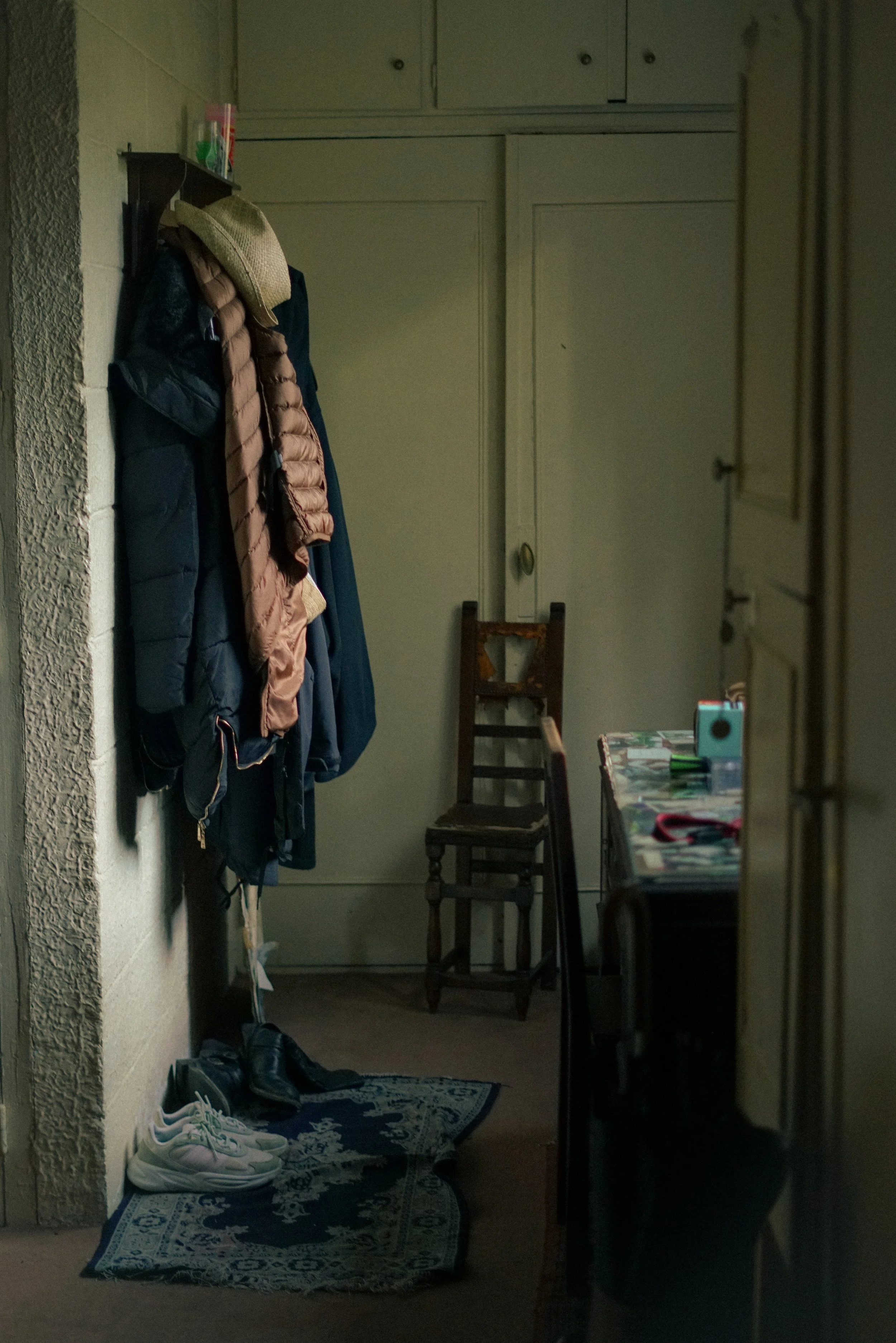 Entrée d'une maison avec manteaux accrochés, chaise en bois, tapis bleu et chaussures posées au sol.