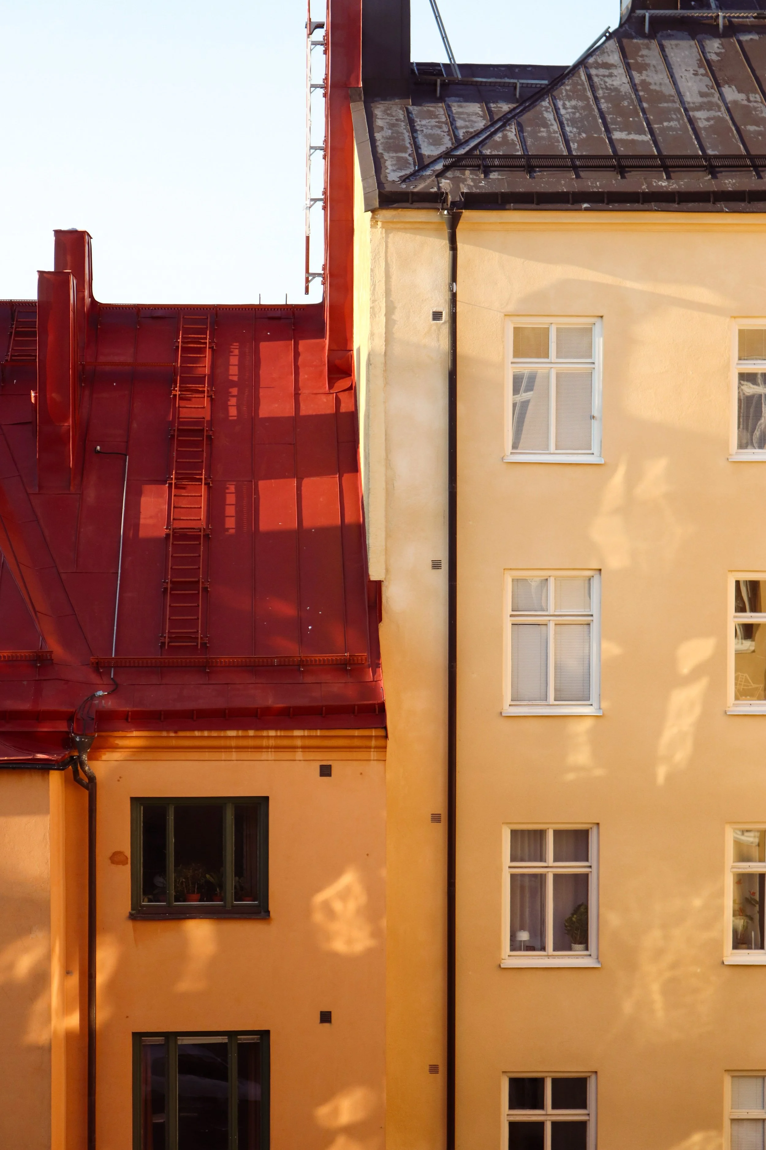 Mur d'un bâtiment jaune avec des fenêtres, toit rouge visible.