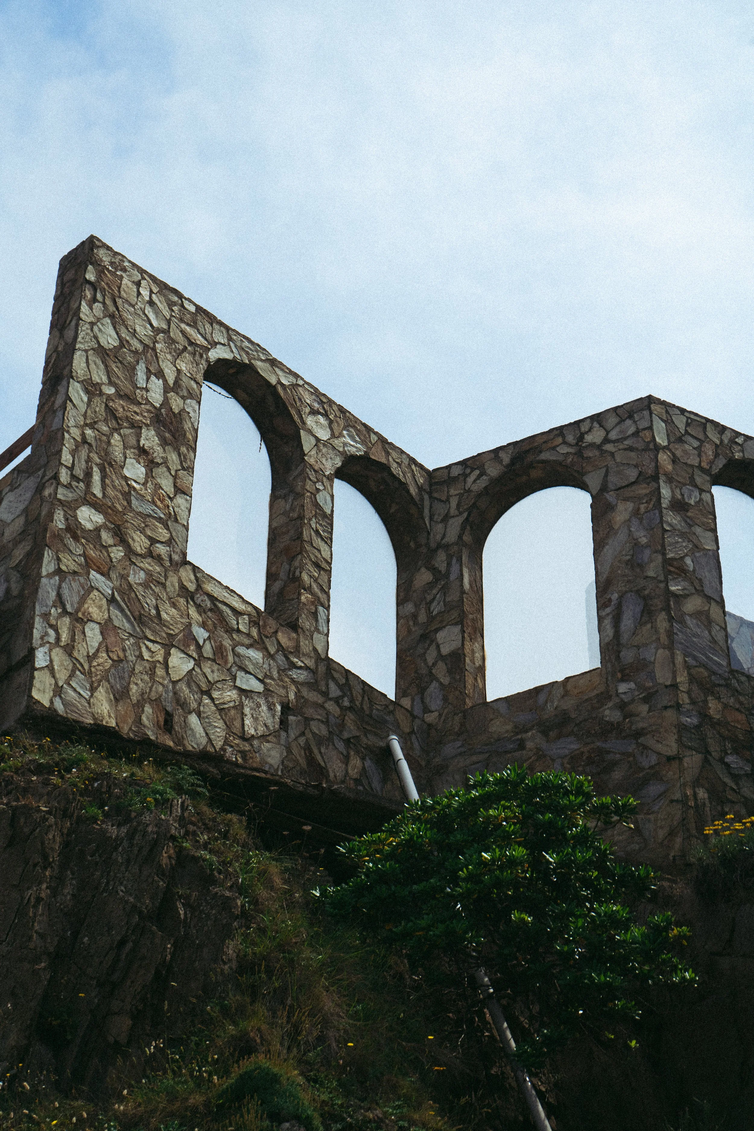 Mur de pierre avec arches sur une colline verdoyante sous un ciel bleu.