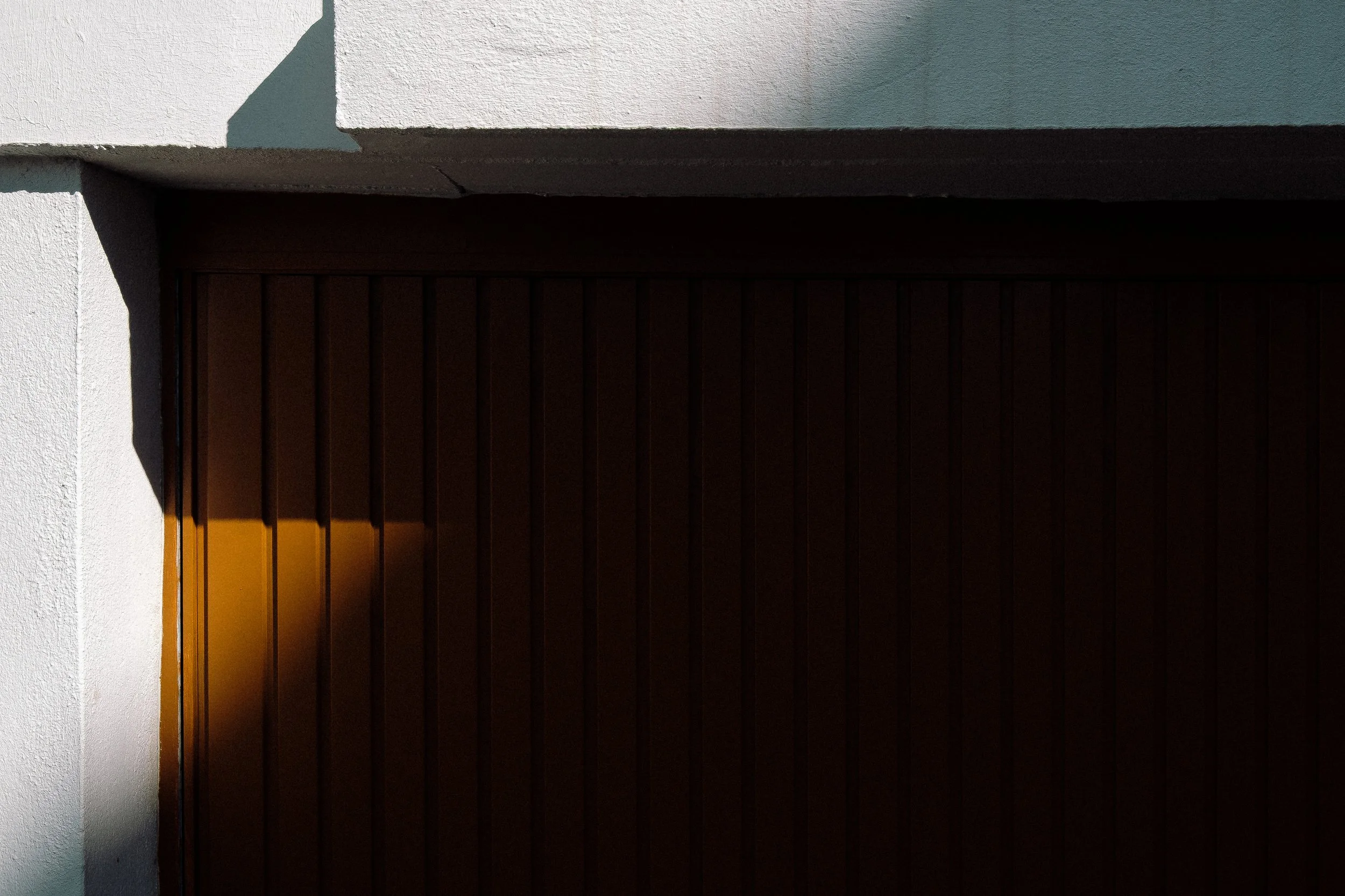 Porte de garage en bois brun avec ombre sur un mur blanc.
