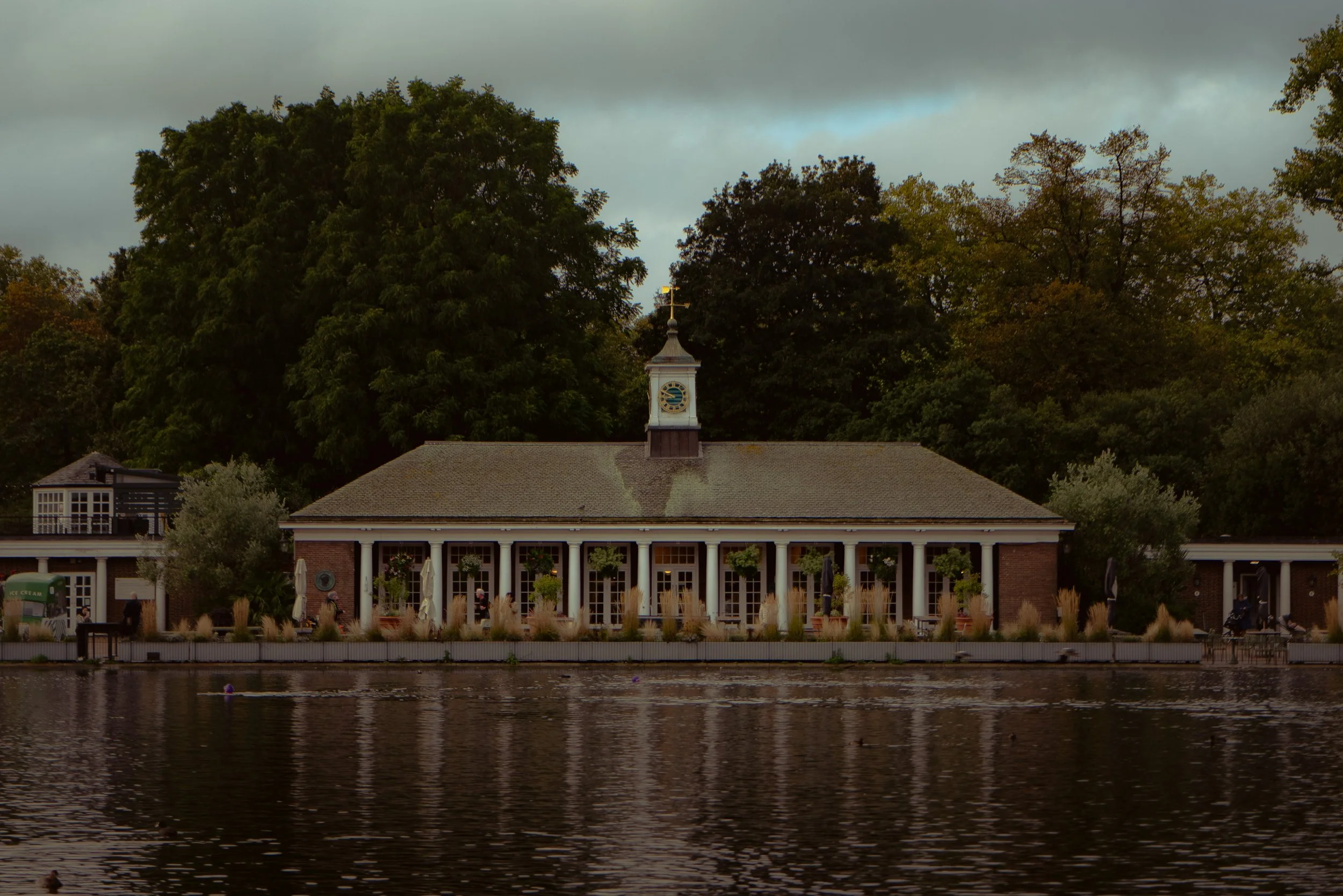 Un bâtiment au bord d'un lac, entouré d'arbres, avec une horloge sur le toit.