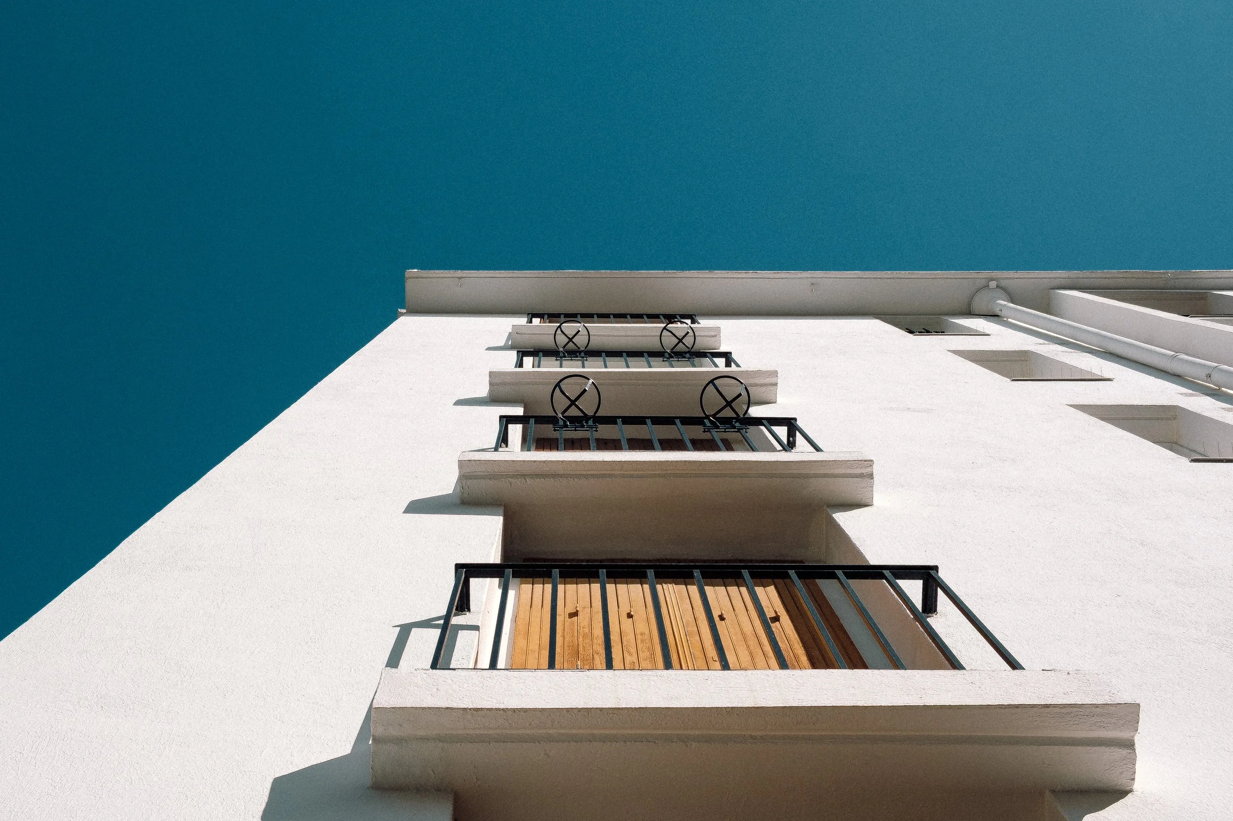 Vue en contre-plongée d'un immeuble blanc avec balcons et ciel bleu clair.