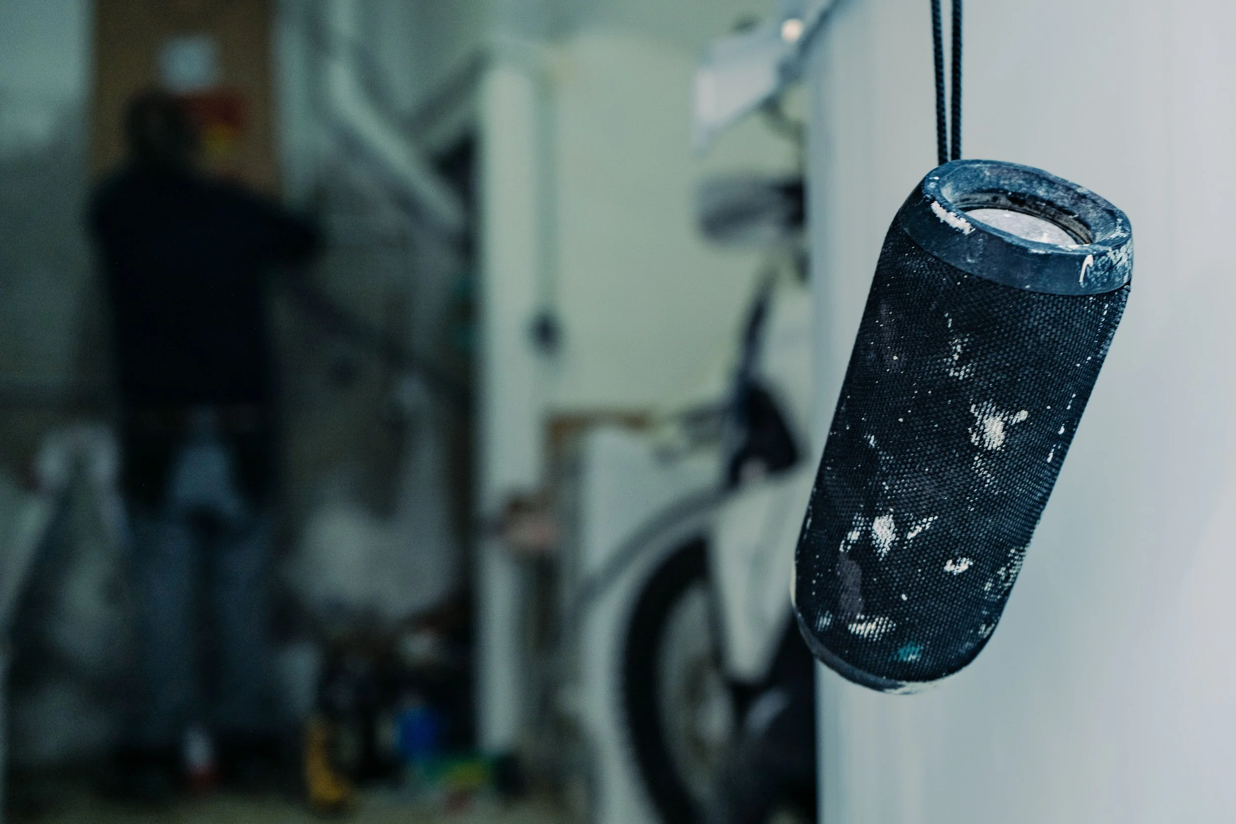 Haut-parleur portable suspendu, arrière-plan flou avec une personne et un vélo.