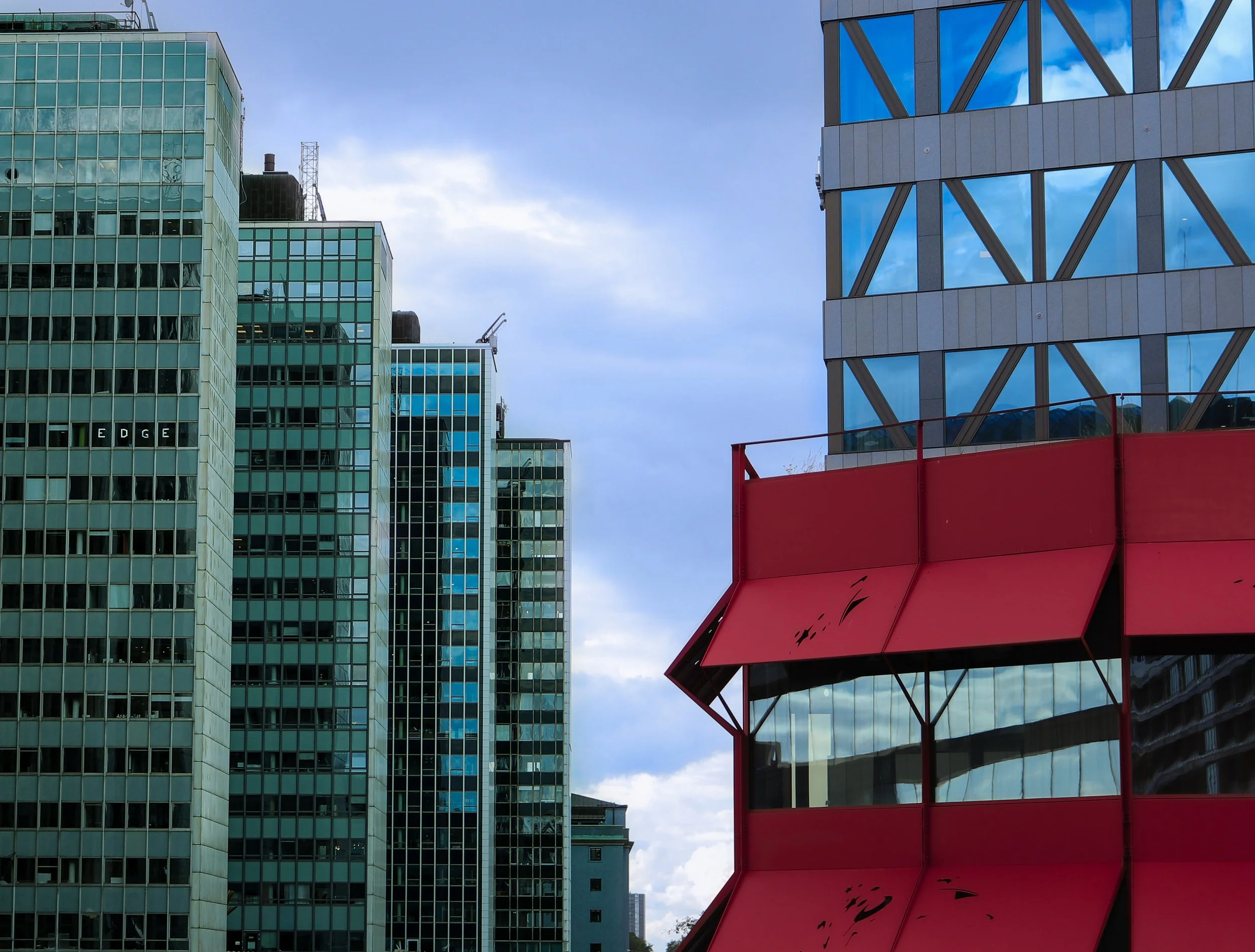 Immeubles modernes et gratte-ciel avec façade en verre, structure rouge et ciel nuageux en arrière-plan.