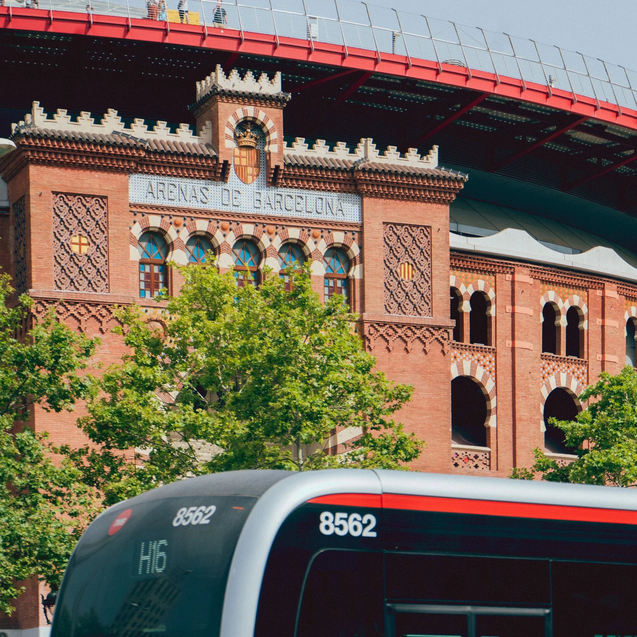 Bâtiment des Arenas de Barcelone avec bus en avant-plan, arbres et ciel bleu.