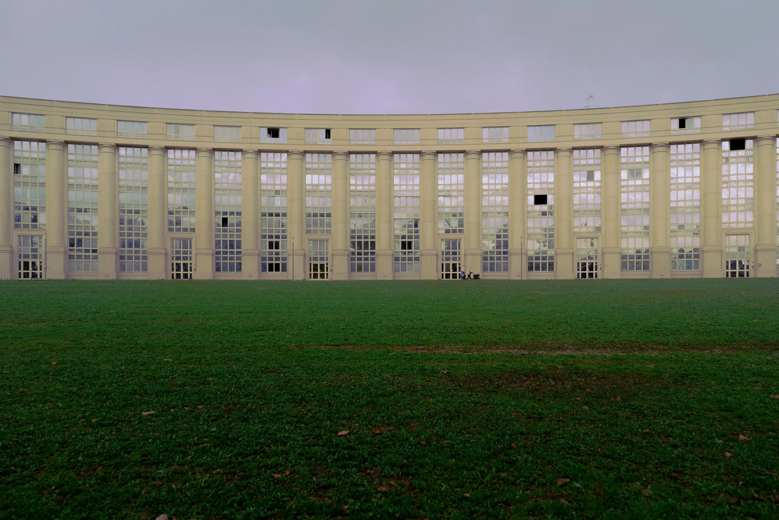 Bâtiment moderne avec de grandes fenêtres symétriques et une pelouse verte à l'avant."