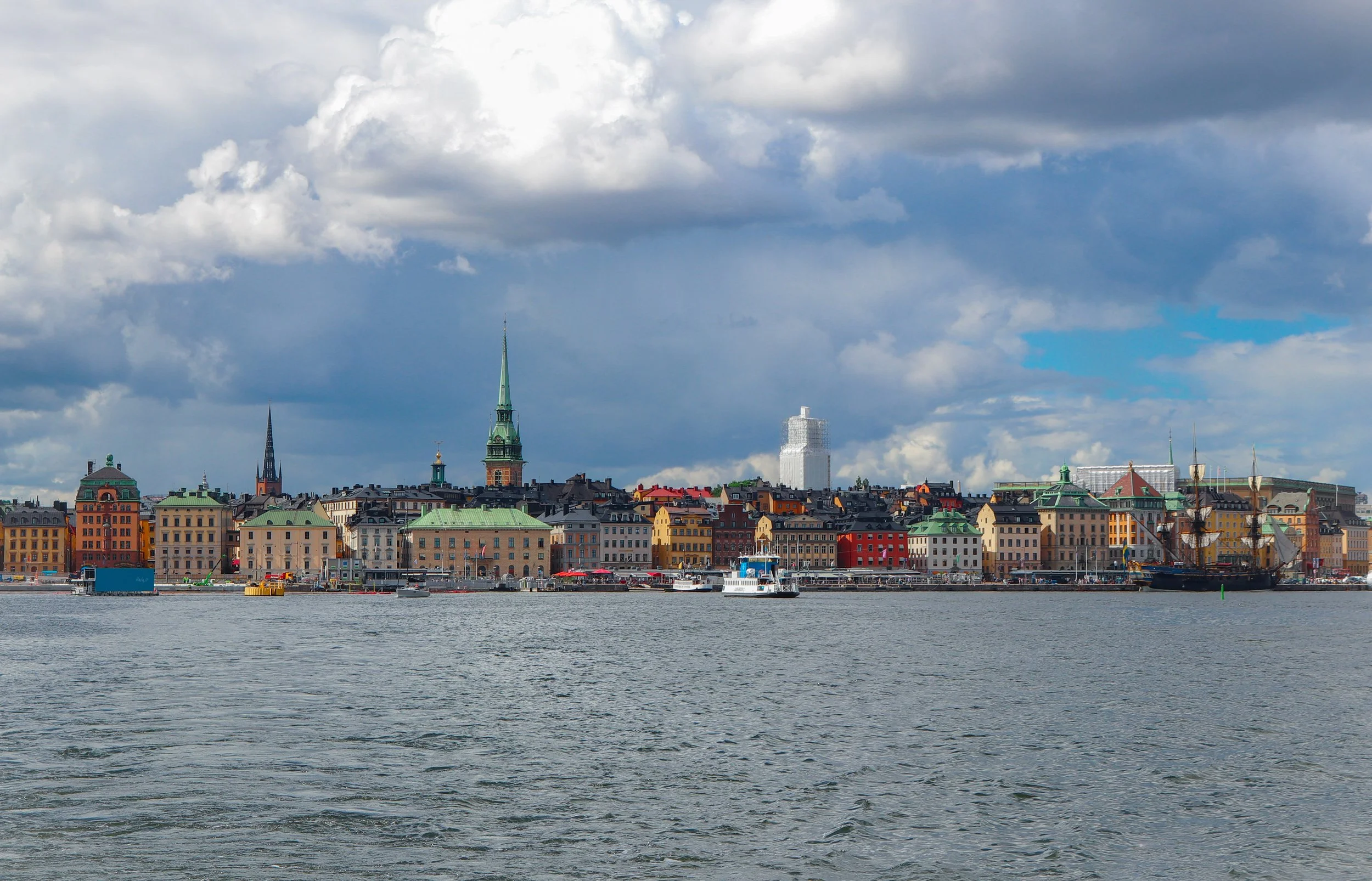 Vue de Stockholm avec bâtiments colorés et un clocher, ciel nuageux, mer au premier plan.