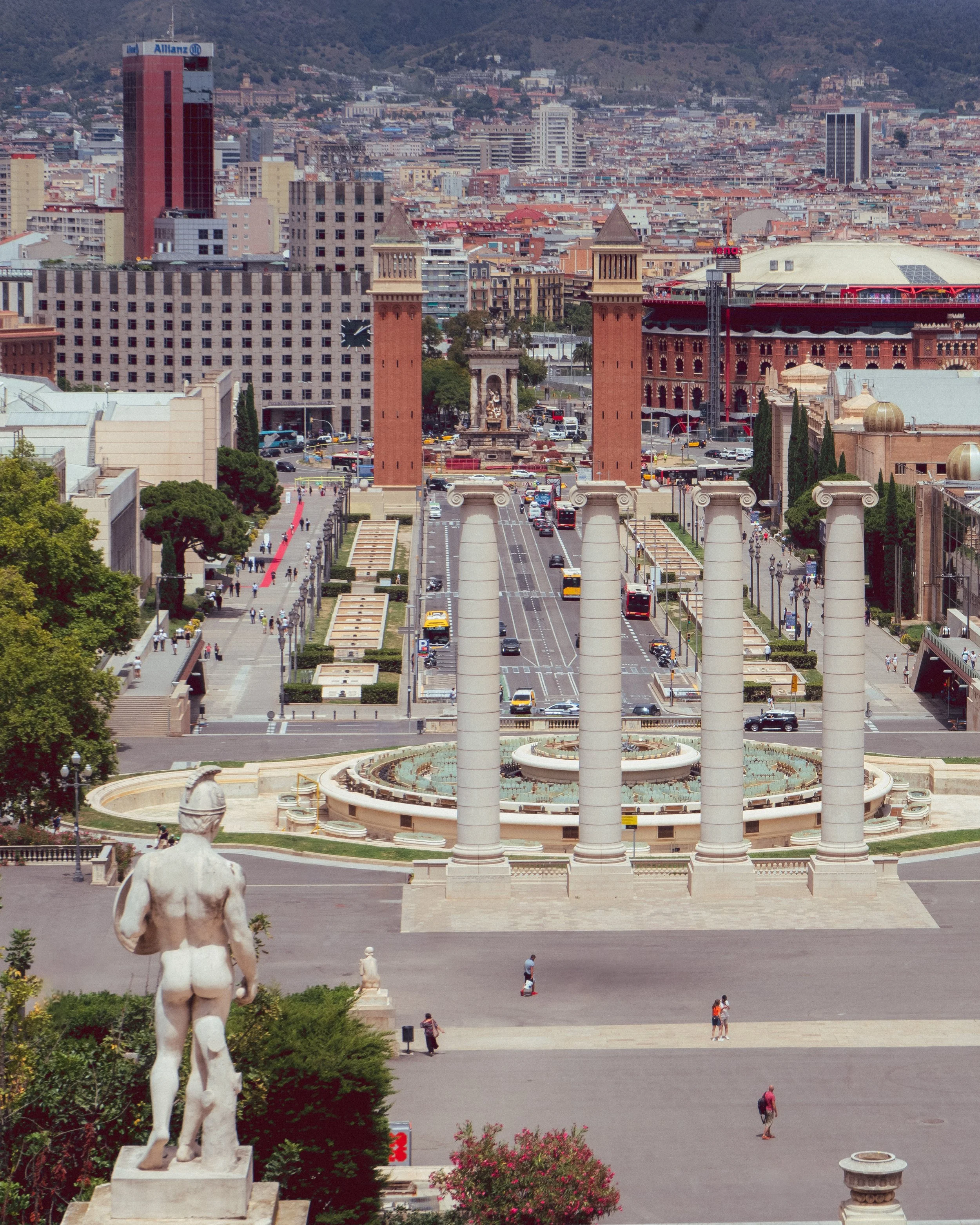 Vue sur Plaça d'Espanya et ses colonnes, Barcelone, avec statue à l'avant-plan et bâtiments en arrière-plan.