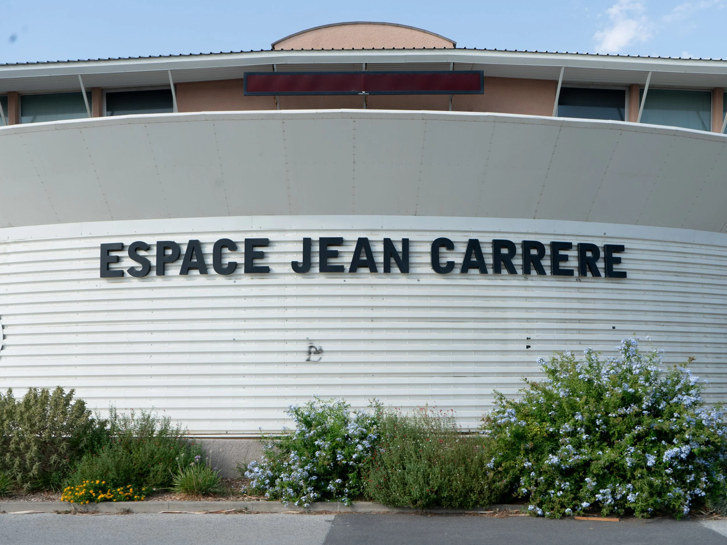 Façade du bâtiment 'Espace Jean Carrere' avec plantes devant.