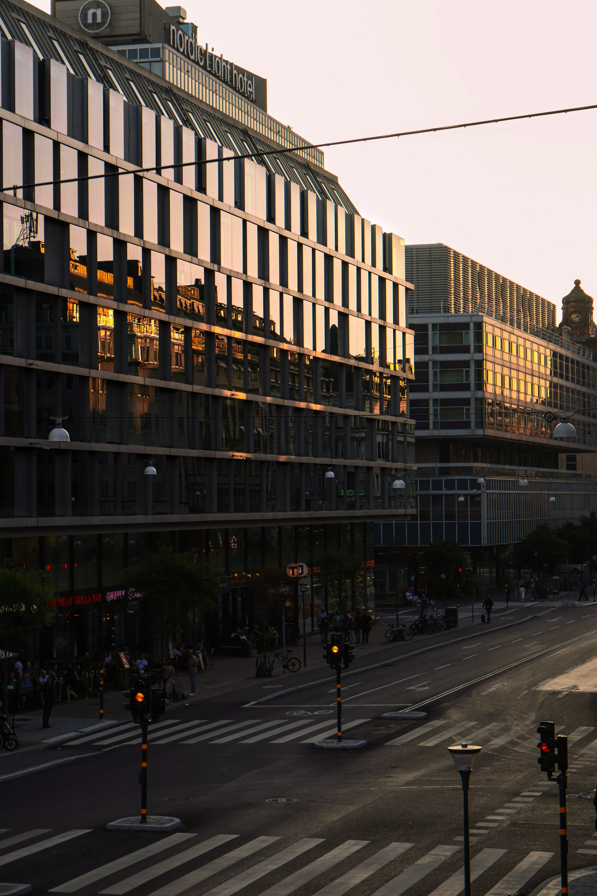 Rue urbaine avec hôtel, bâtiments modernes et passage piéton au coucher du soleil.