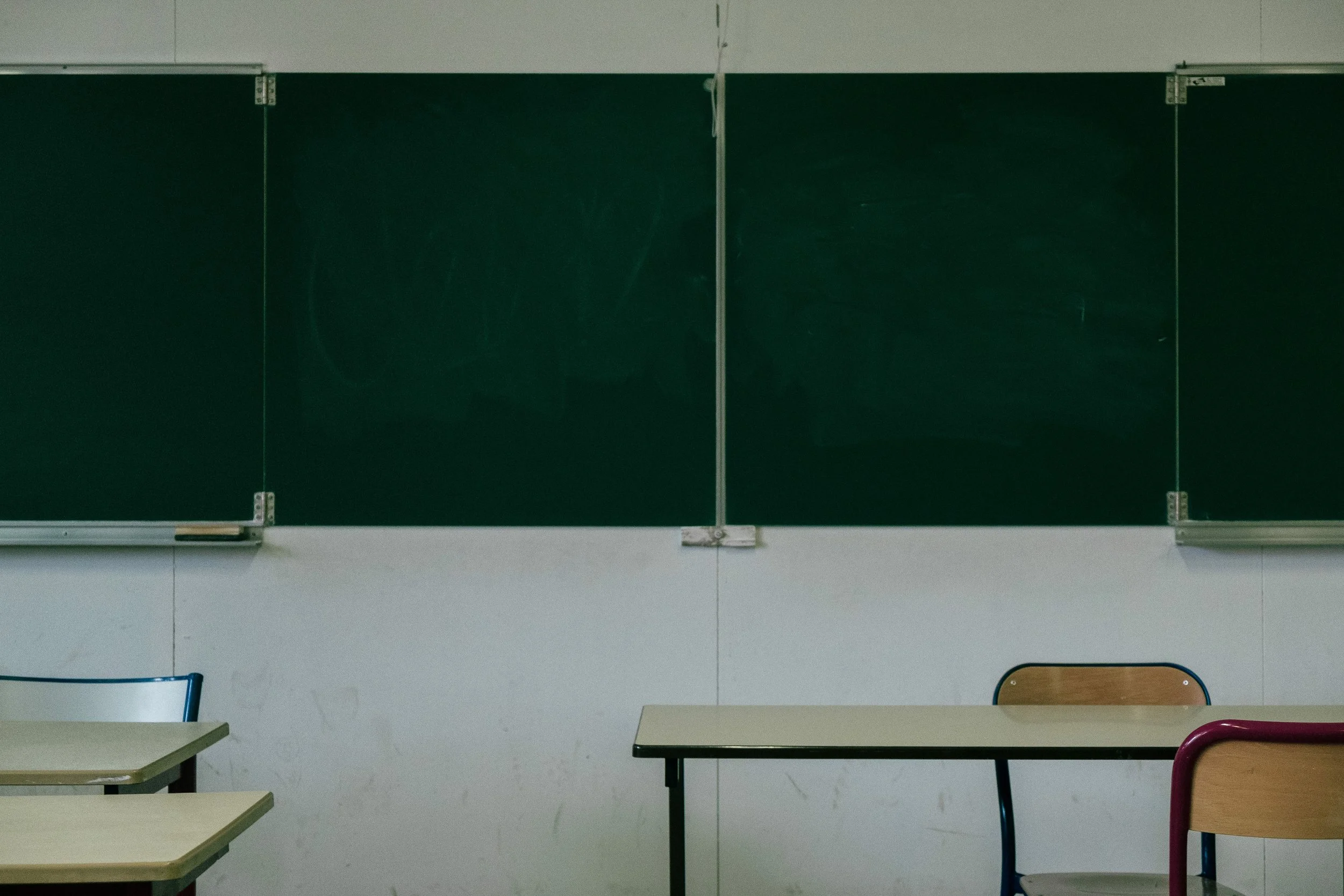 Salle de classe avec tableau noir, tables et chaises vides.