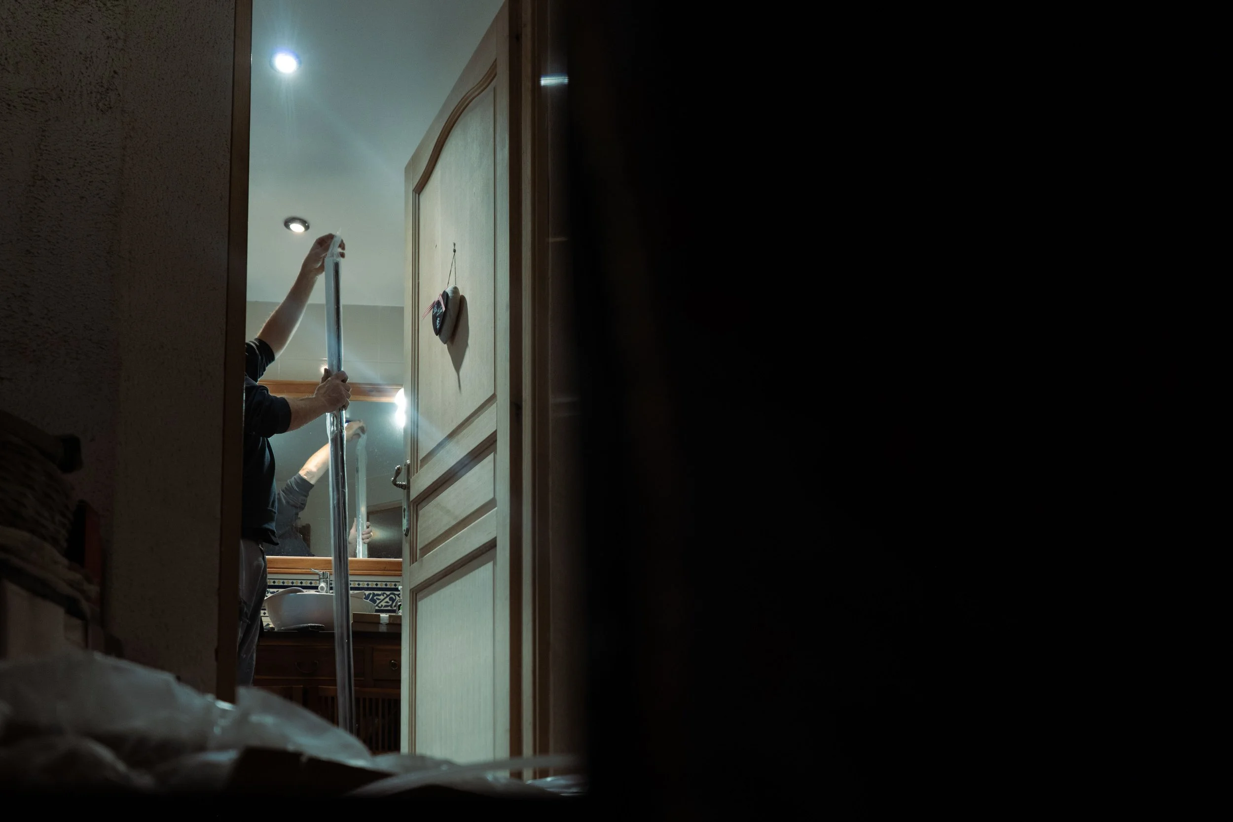 Personne installant une porte ou un panneau, vue à travers une ouverture sombre, avec de la lumière dans la pièce.