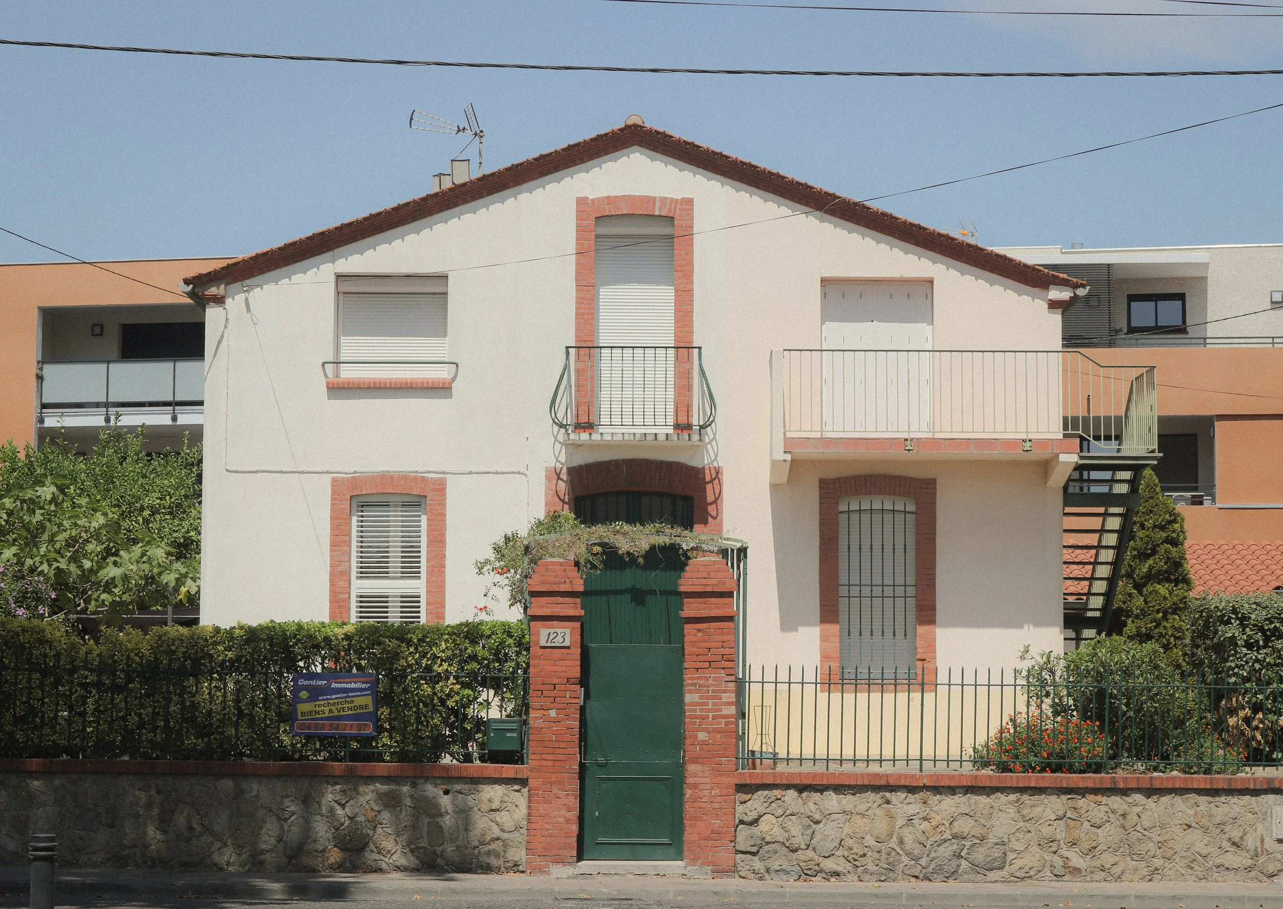 Maison à deux étages avec grille verte et jardin, à vendre, architecture traditionnelle.