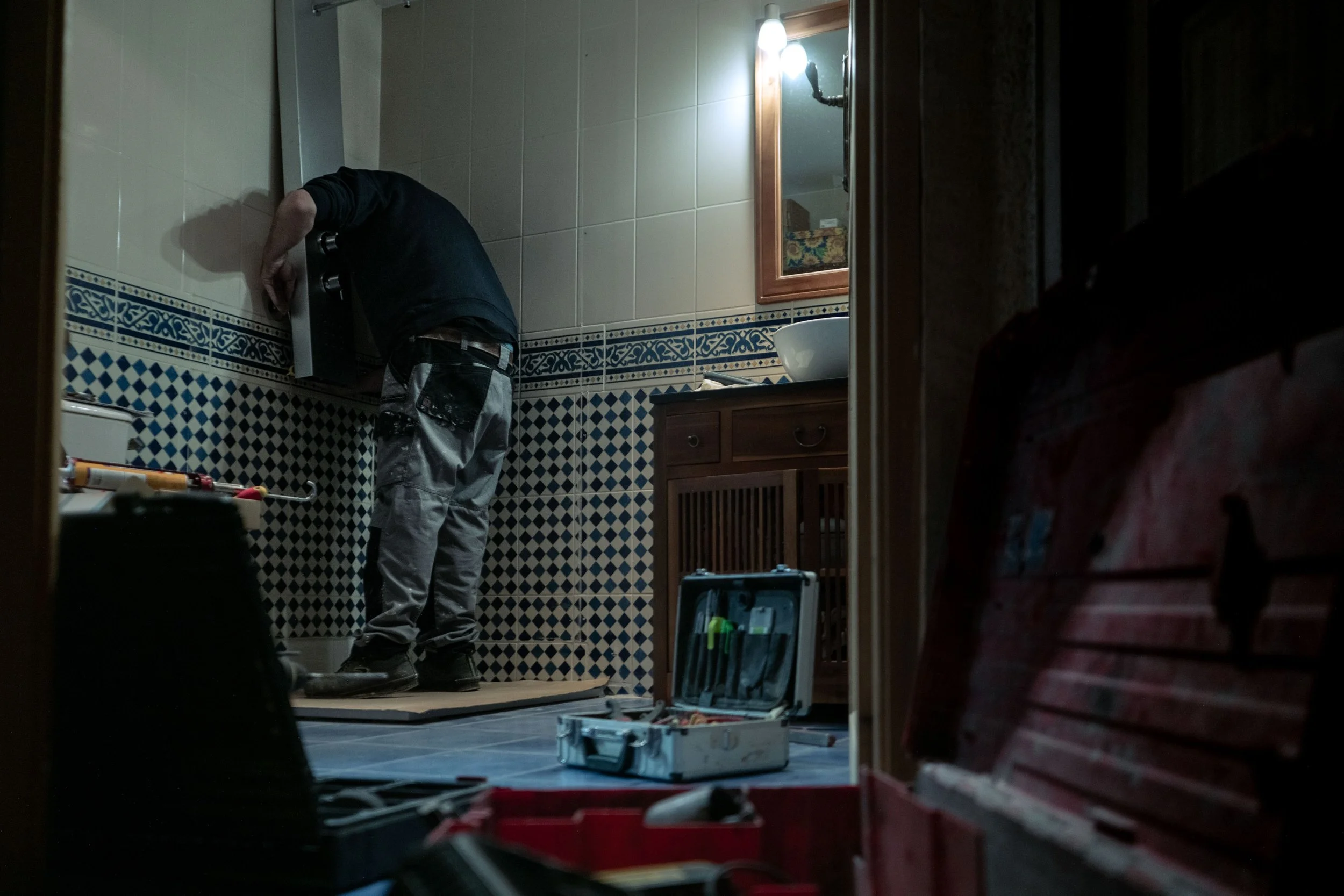 Une personne effectuant des travaux de plomberie dans une salle de bain avec outils et carreaux de faïence.