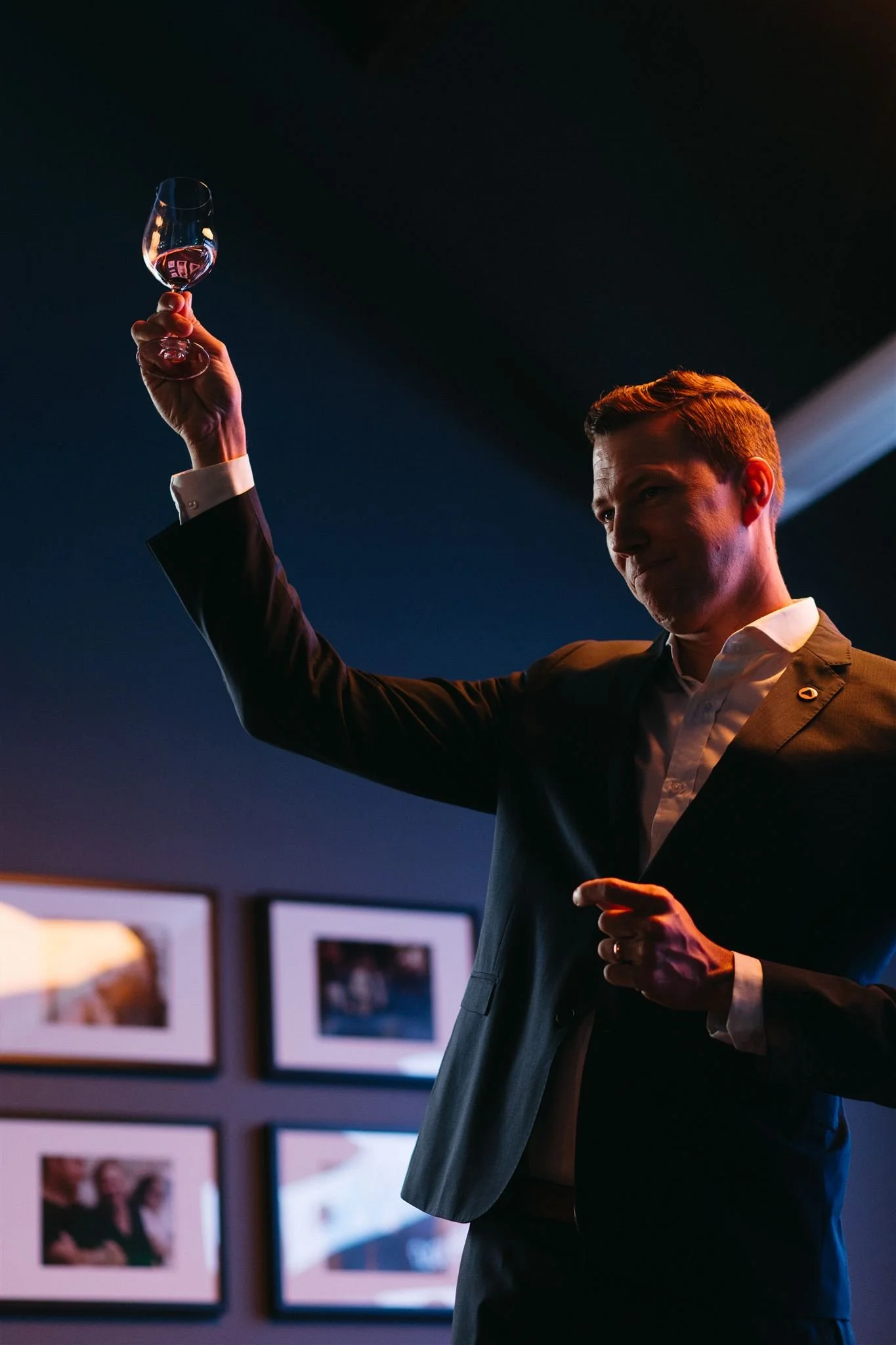 A man in a suit raising a wine glass for a toast under dramatic lighting at a London corporate gala dinner.