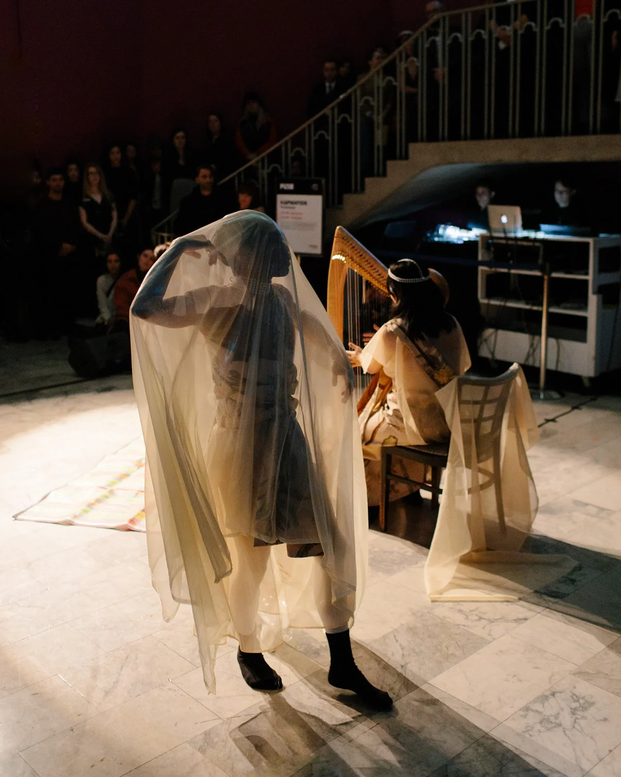 A dancer in a sheer white veil performing alongside a harpist at a contemporary London art gallery event.